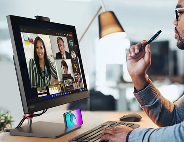 Office manager on a conference call via a ThinkCentre Neo 50a all-in-one PC, with phone (sold separately) in phone holder, and pen (sold separately) in his hand.