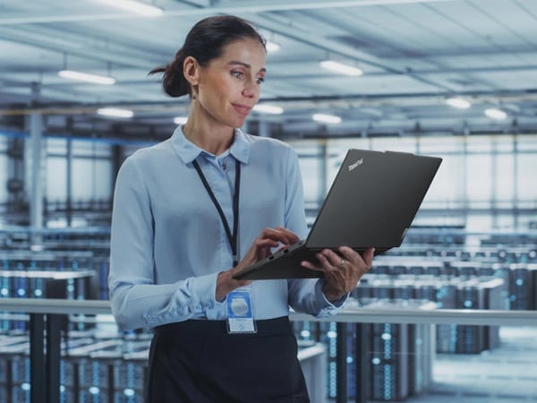 Person standing in data center, holding ThinkPad E14 Gen 5 (14" Intel) laptop in one hand and looking at the display