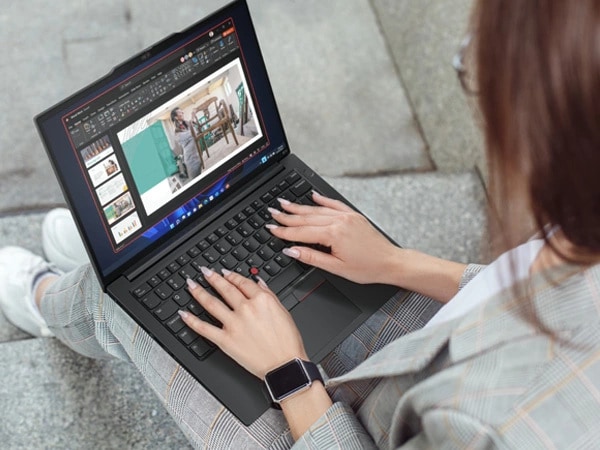 Over-the-shoulder, close-up view of person sitting on concrete stairs, holding ThinkPad E14 Gen 5 (14" Intel) laptop in their lap, with both hands on keyboard, looking at slideshow on the display